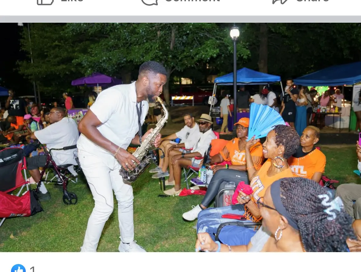 Man playing saxophone for seated audience outdoors.