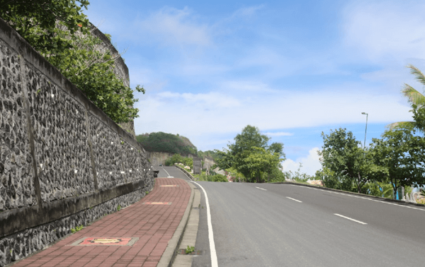 Empty road beside stone wall and trees.