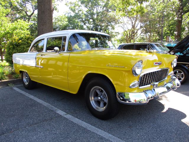Yellow classic car parked under trees.